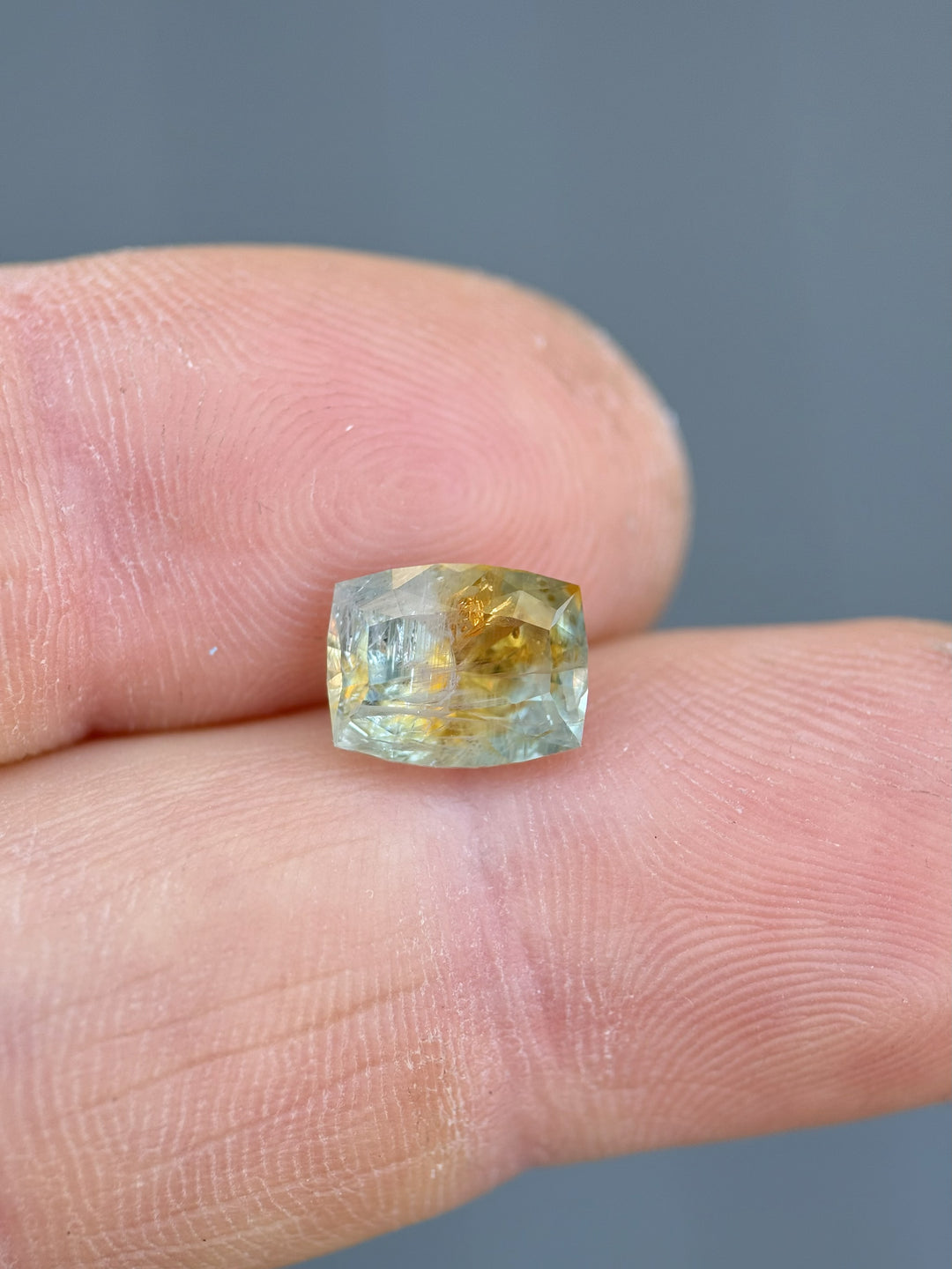 Close-up of 2.99 carat Montana sapphire resting on a fingertip, highlighting its custom elongated cushion shape and vibrant teal-orange parti colors.