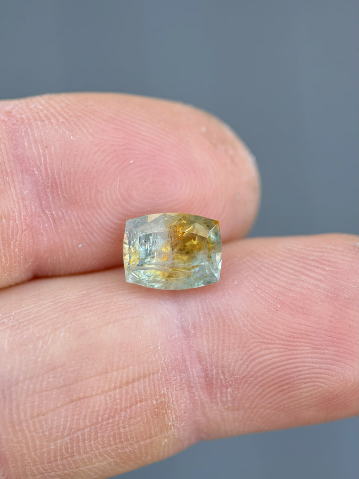 Close-up of 2.99 carat Montana sapphire resting on a fingertip, highlighting its custom elongated cushion shape and vibrant teal-orange parti colors.