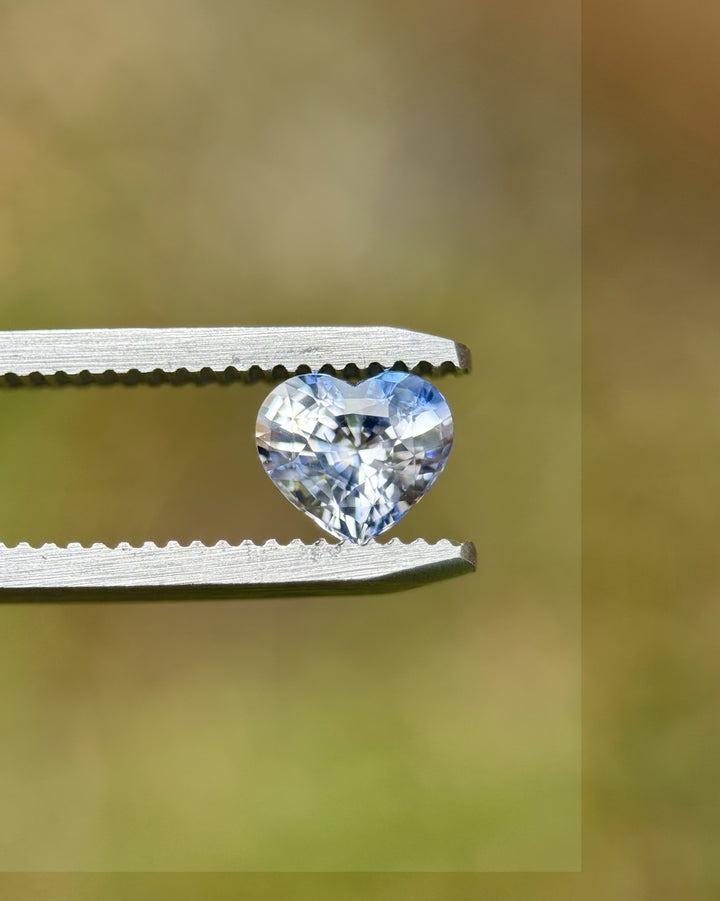 Heated 1.30-carat heart cut parti sapphire held by tweezers, showcasing its vivid blue and icy white color zones from Sakaraha, Madagascar.