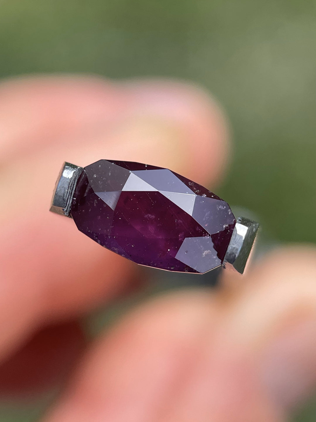 Close-up of a 3.81-carat raspberry plum sapphire held by tweezers, showing its elongated double rose cut and vivid saturation.