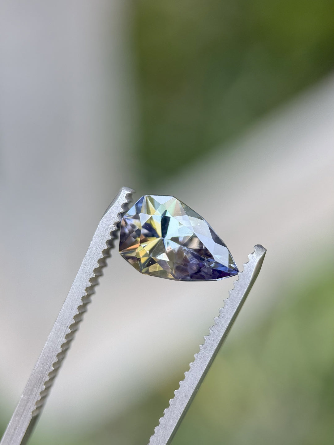 2.46ct Tanzanite with vibrant green, purple, and teal flashes held in gemstone tweezers – untreated pear cut gem from Tanzania