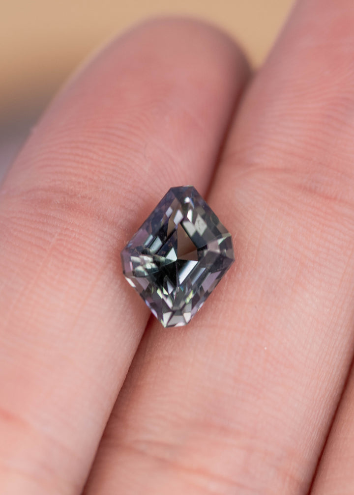 2.81 carat mermaid violet blue teal green Tanzanite resting on fingers showing custom geometric step cut parallelogram faceting and color shift