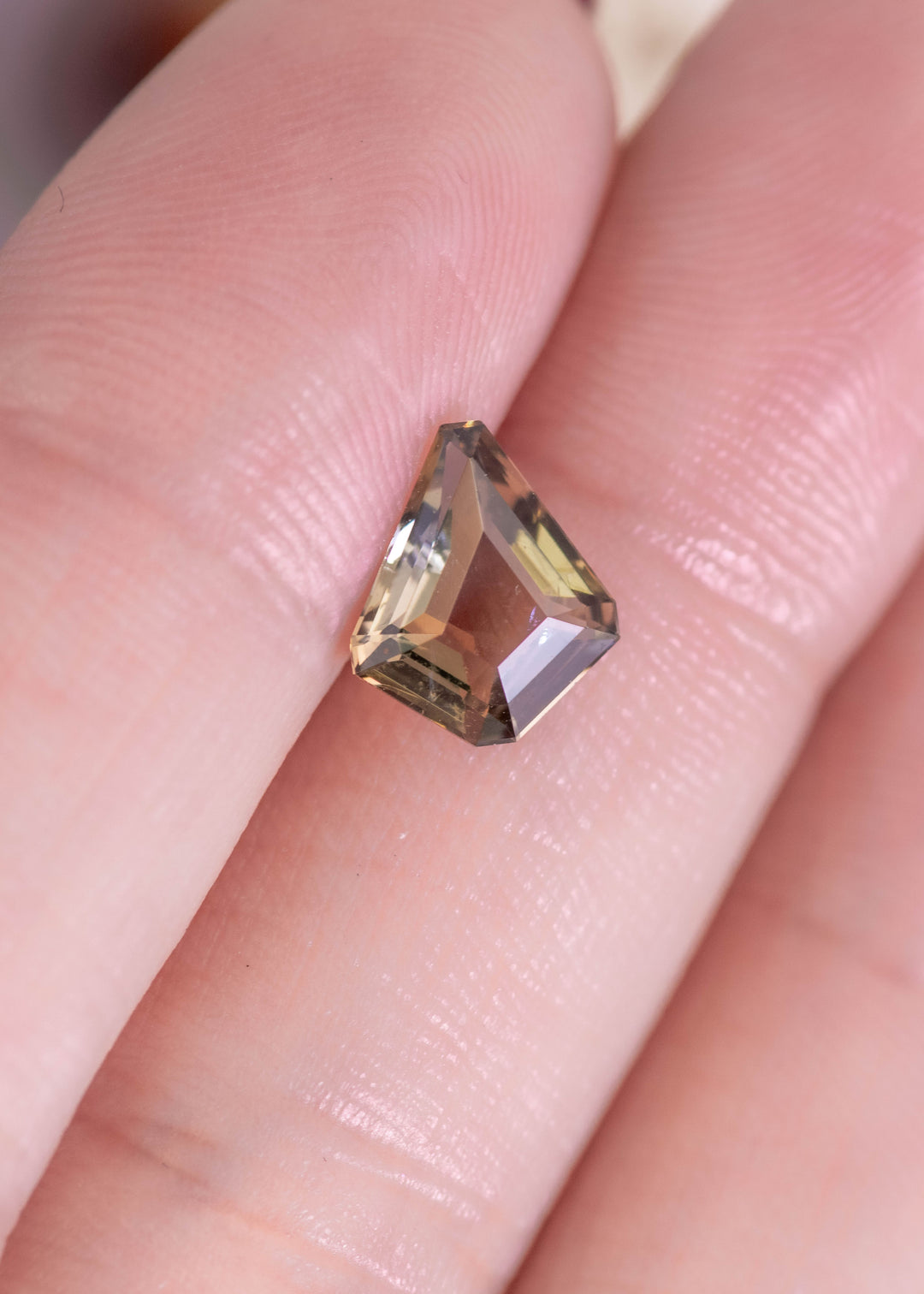 Loose 1.72ct Tanzanite kite cut gemstone resting on fingers displaying golden brown and yellow color shift from Merelani Hills Tanzania
