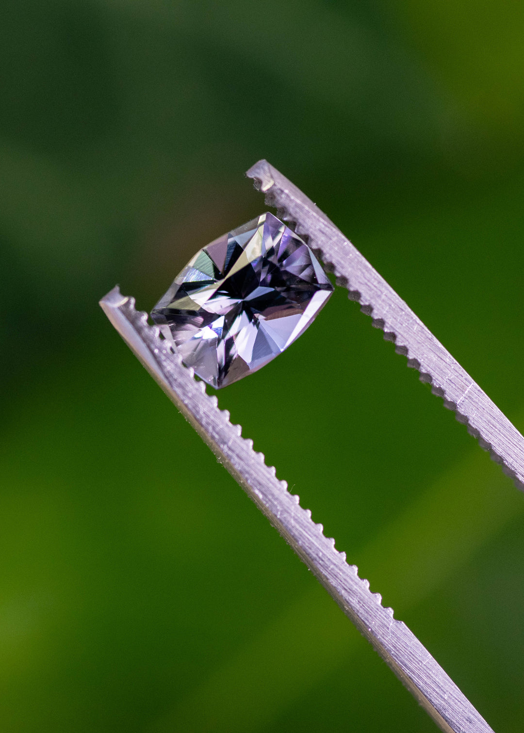 Close-up of an untreated 1.54 carat mermaid tanzanite held in tweezers, showcasing a custom mix cushion cut with purple, blue, and green tones from Merelani Hills, Tanzania.