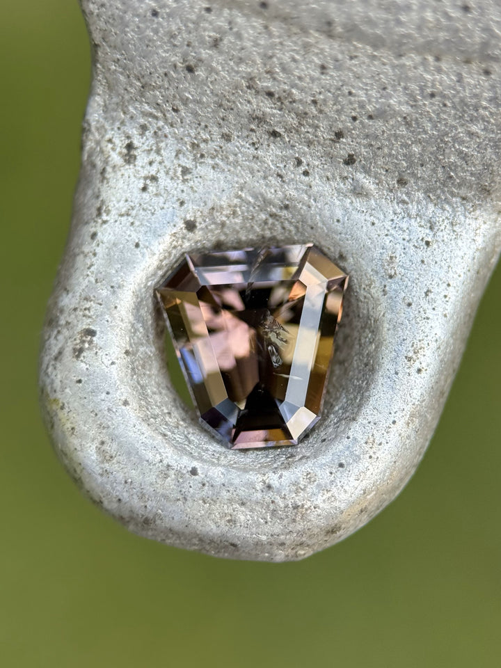 Multicolored 1.68CT Tanzanite in shield cut resting on textured metal surface.