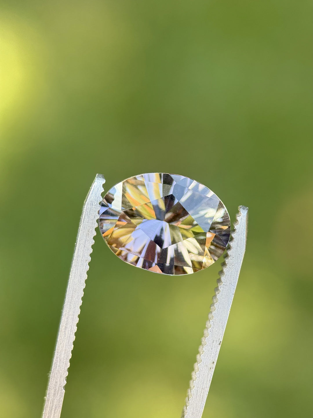 Fancy multicolor Tanzanite gemstone in tweezers, showcasing peach, teal, purple, and yellow tones in an intricate oval concave cut, 4.78 carats from Merelani Hills