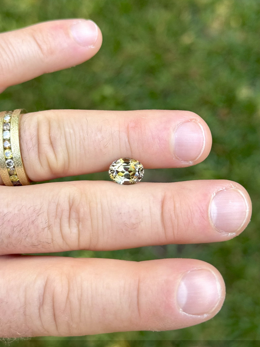 Fancy Tanzanite gemstone resting on fingers outdoors, showcasing its oval cut and multi-color brilliance