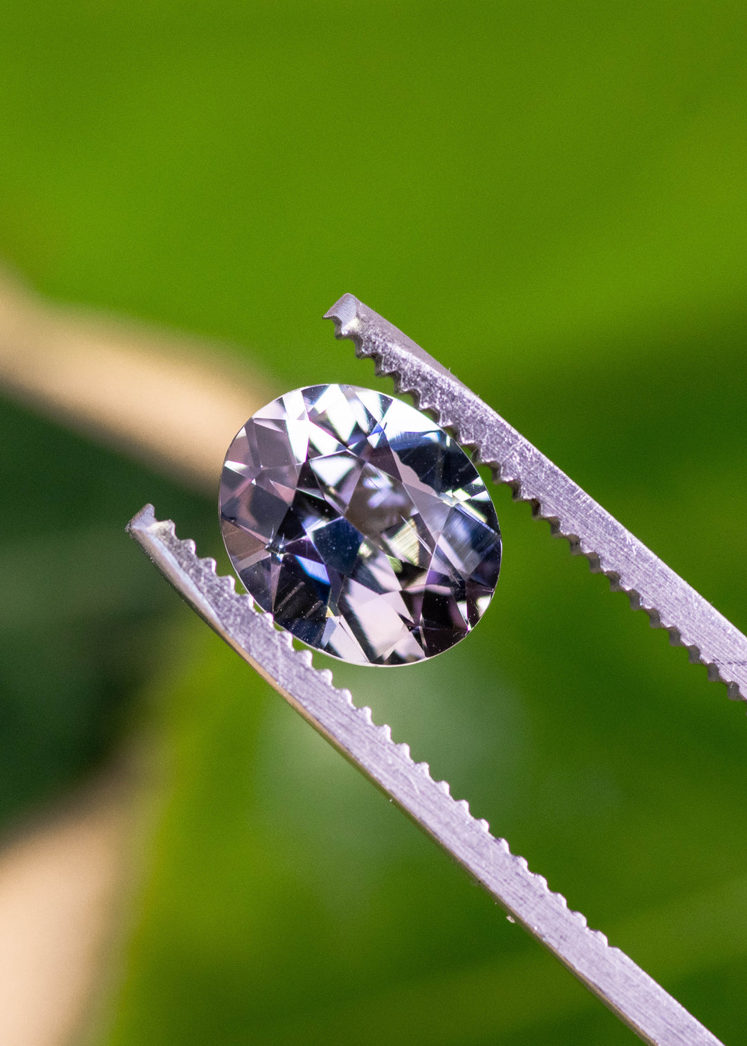 Close-up of a 2.57 carat Tanzanite held in gem tweezers, highlighting crisp brilliant facets and a teal blue lavender color blend in a custom oval cut, untreated gemstone from Merelani Hills, Tanzania