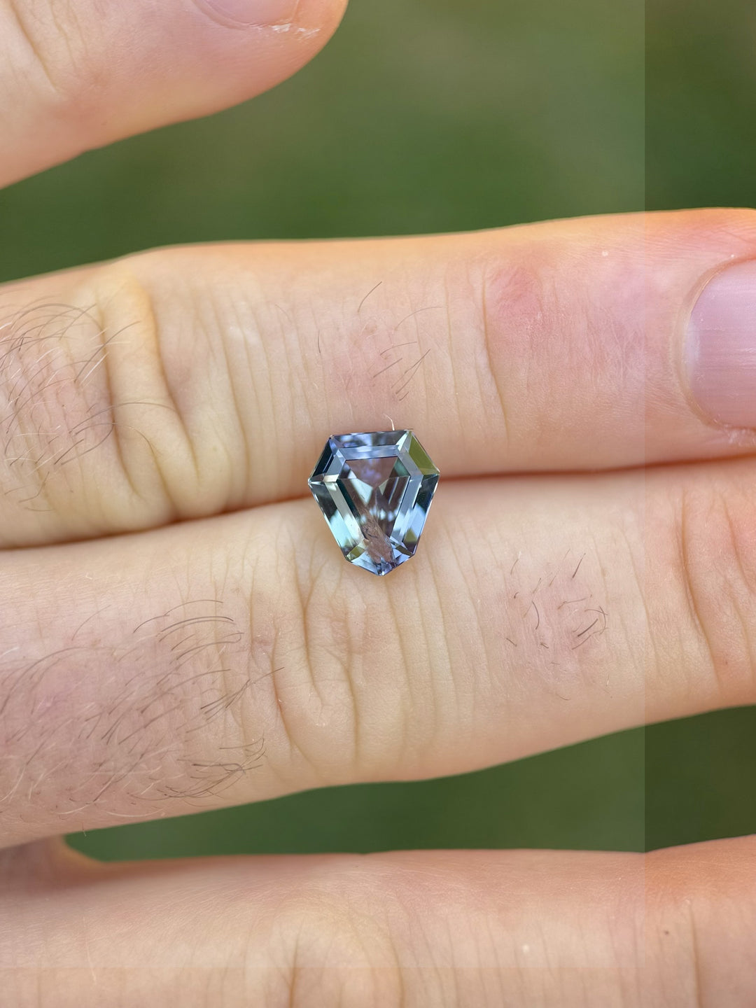 Tanzanite 2.75ct custom shield cut displayed on fingertips to showcase size and sparkle under natural lighting