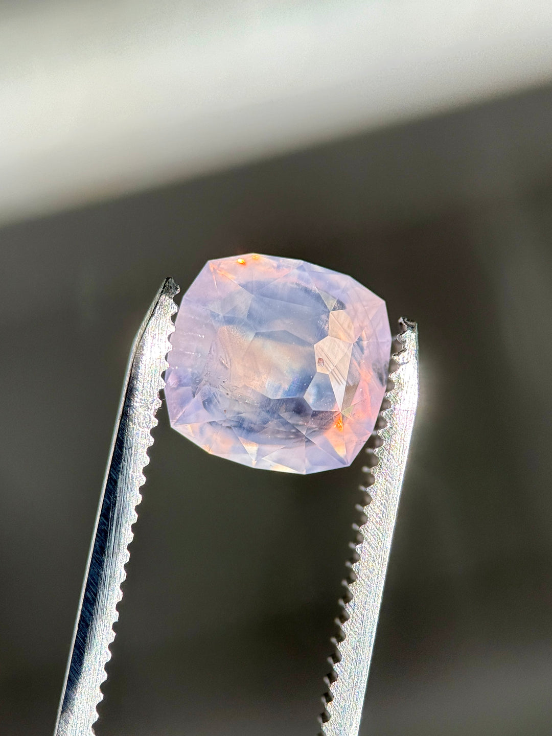 Faceted 5.12 carat opalescent pink sapphire held in tweezers against a dark background