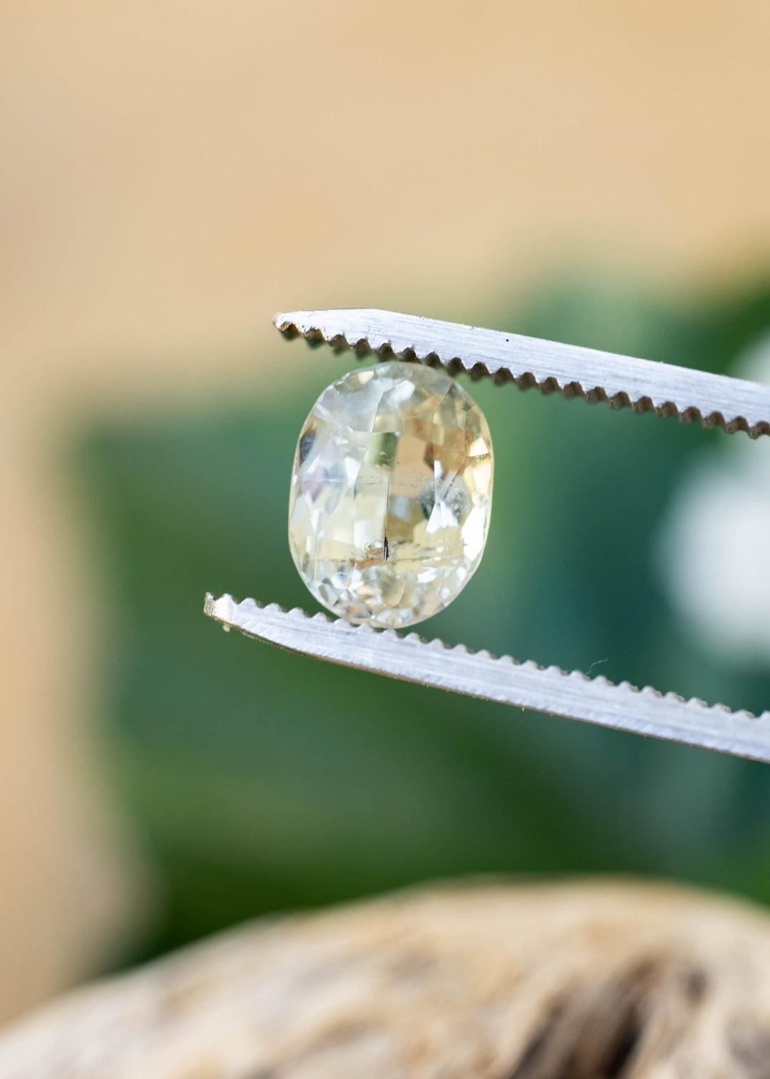 2.37 carat pale yellow tourmaline held upright between jeweler’s tweezers, showing its vintage oval brilliant mix cut, translucent body and natural internal inclusions.