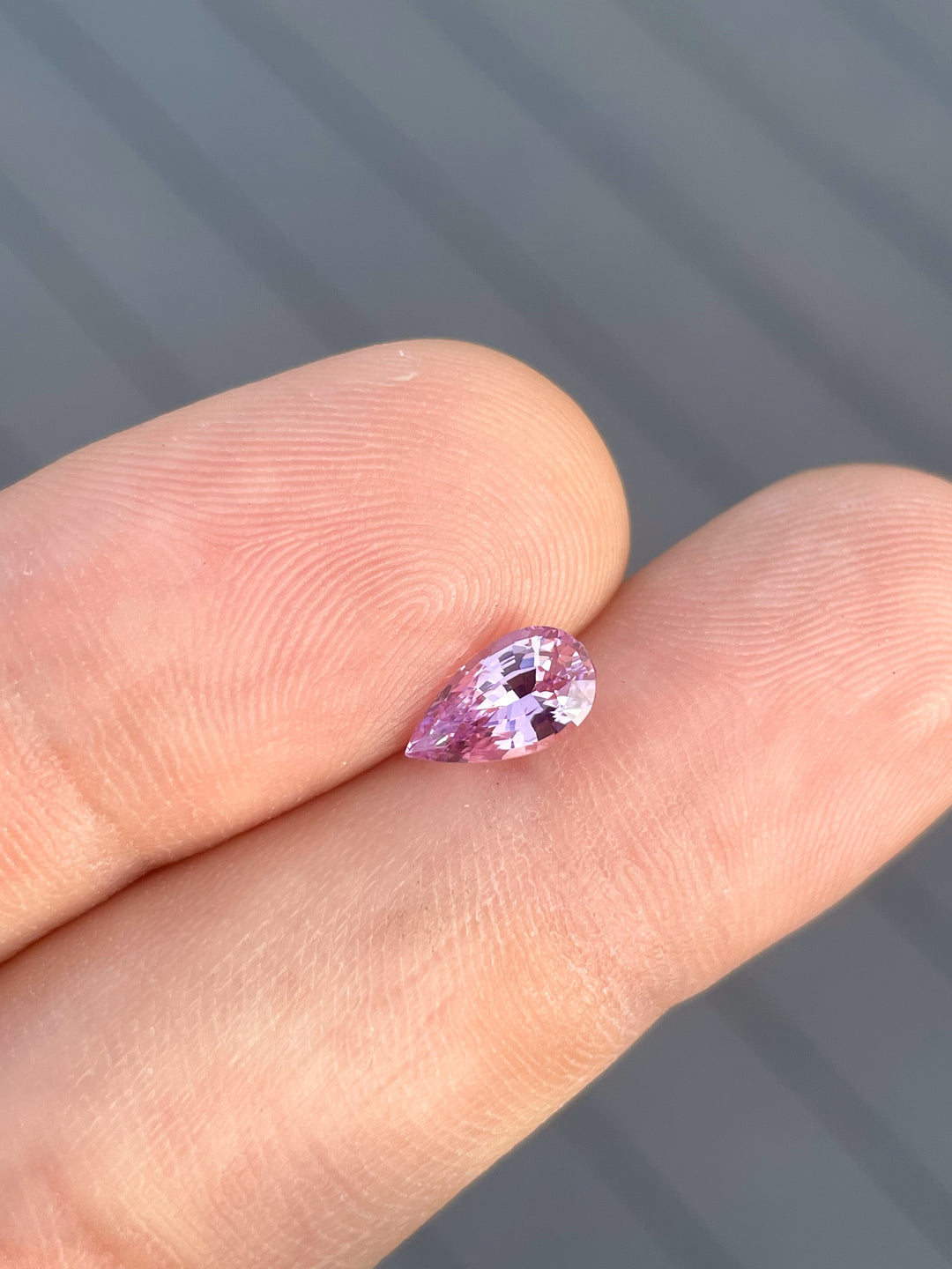 A 1.54-carat purple sapphire in pear shape, held gently on a fingertip, highlighting its vibrant color and fine brilliance. This gemstone from Sri Lanka is untreated and expertly cut for maximum sparkle.