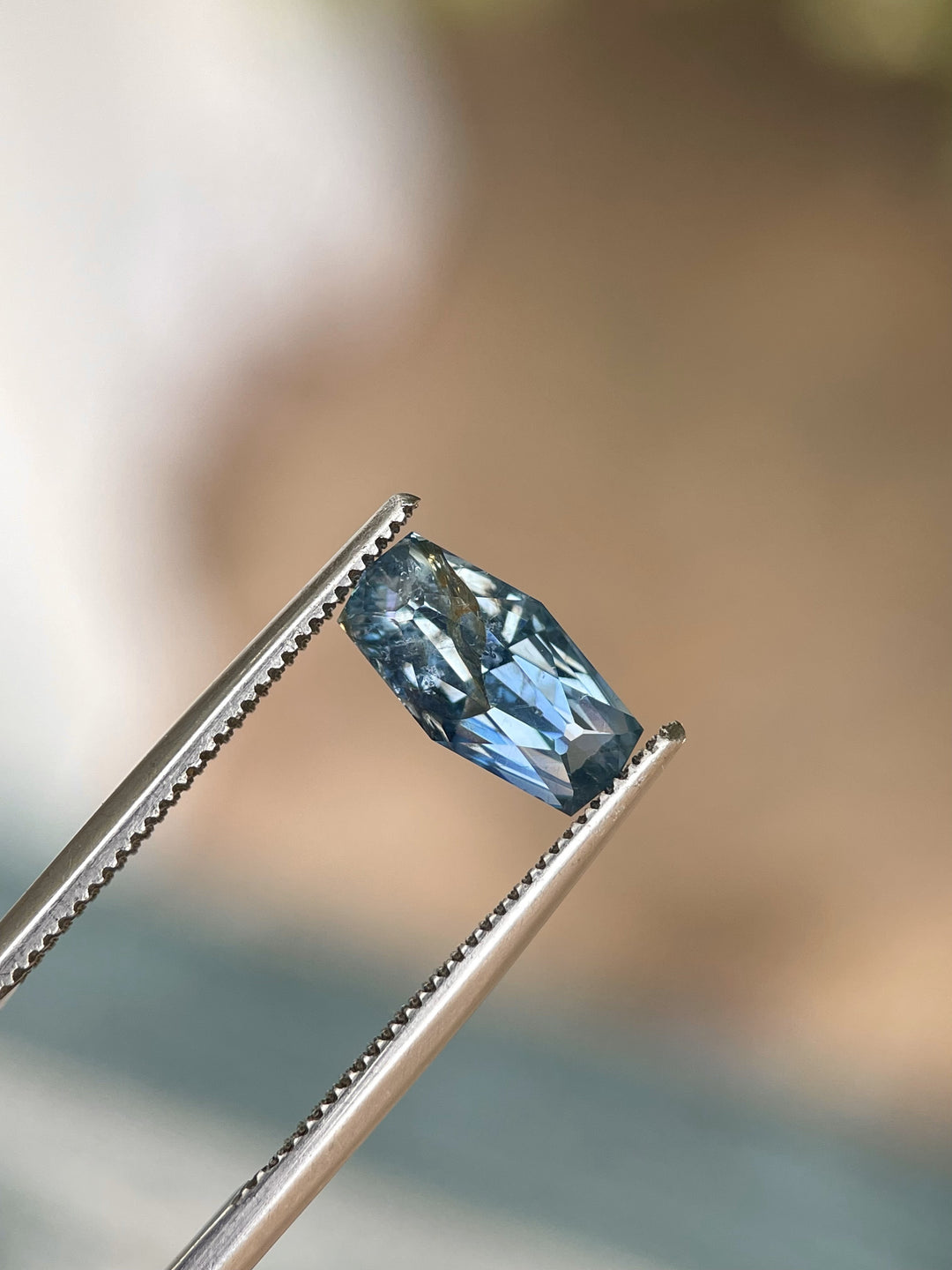 A 2.14-carat denim blue sapphire with a custom geometric elongated cushion cut, held by tweezers, revealing its precise cut and vibrant blue color. The gemstone from the Umba River, Tanzania, is untreated and measures 10.66mm by 5.55mm by 4.17mm.