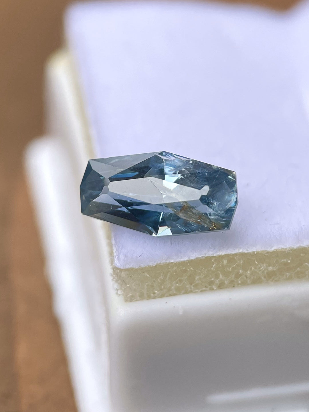 A 2.14-carat no heat denim blue sapphire with a custom geometric elongated cushion cut, displayed on a velvet surface. The gemstone reflects its rich denim blue tones and crisp facets. Sourced from the Umba River, Tanzania, it measures 10.66mm by 5.55mm by 4.17mm and is untreated.