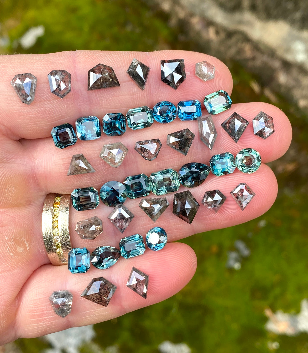 Hand holding blue, teal, gray, and rose cut loose gemstones selected for custom jewelry, client projects, and designer sourcing.