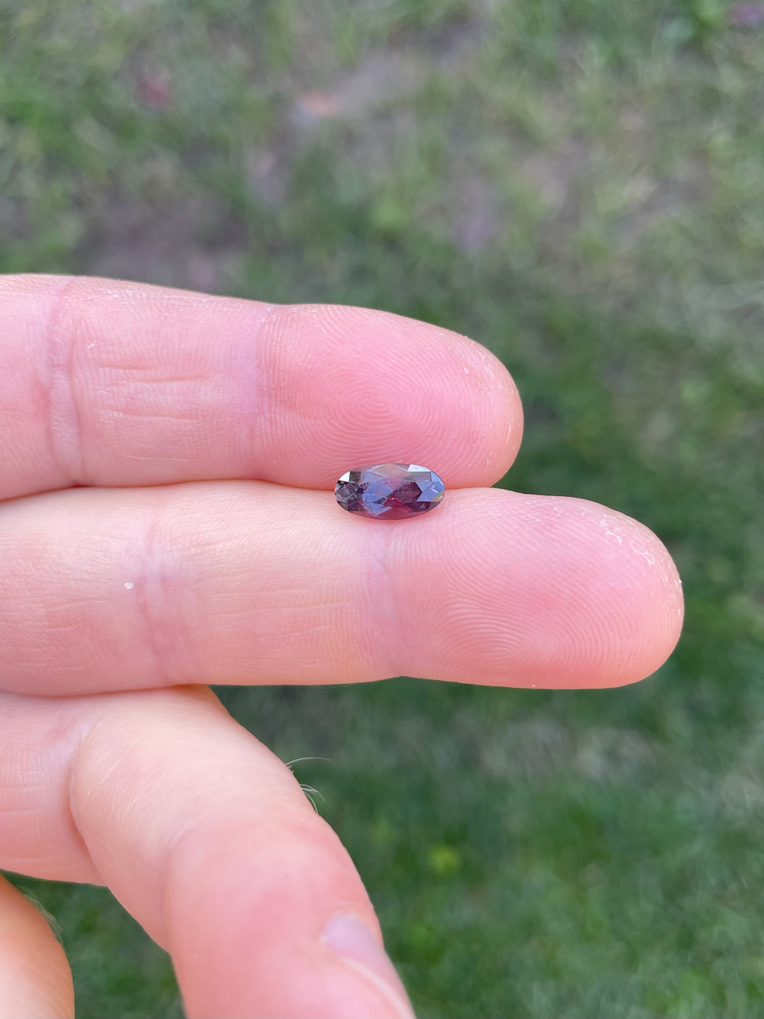 1.63-carat unheated sapphire in dusty rose and mauve, displayed on fingertips. Moval cut gemstone from Umba River, Tanzania.
