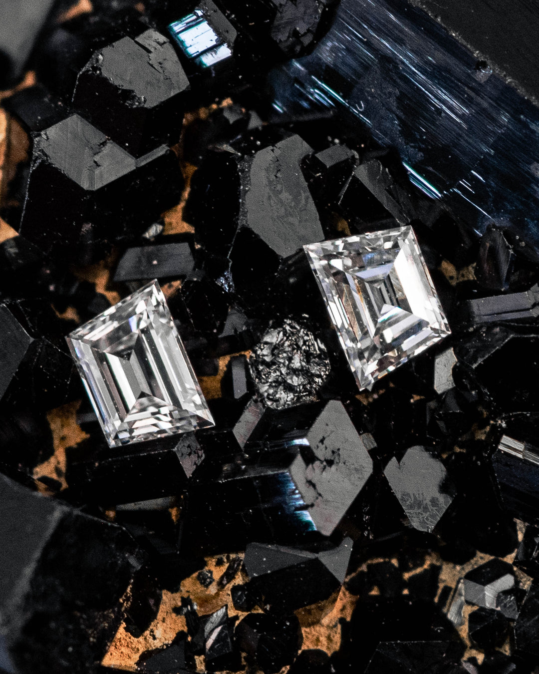 0.18 carat E color VVS clarity Trapezoid step cut diamonds resting on a black crystal mineral matrix, highlighting the sharp step-cut facets and matched proportions of the two South African diamonds.