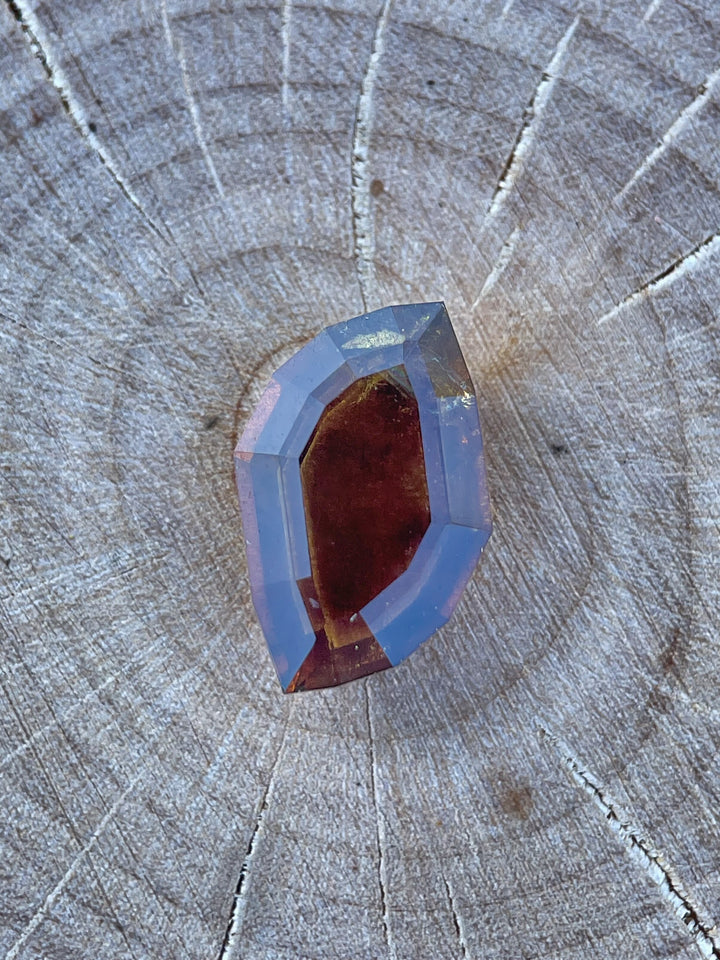 Close-up of a 3.78-carat earthy brown cognac sapphire with a custom leaf portrait cut, placed on a wooden background to highlight its intricate design and natural tones. Origin: Umba River, Tanzania, untreated gemstone.