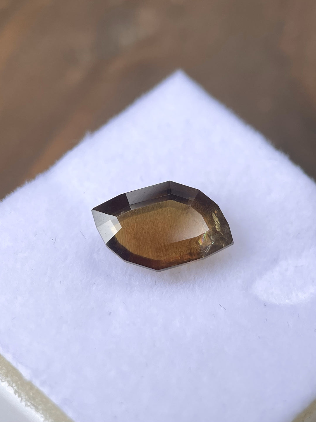 A 3.78-carat earthy brown cognac sapphire with a custom leaf portrait cut, displayed on a white velvet surface. The gemstone showcases warm brown hues and intricate facets. Sourced from the Umba River, Tanzania, the sapphire is untreated and measures 12.76mm by 4.78mm by 3.80mm.