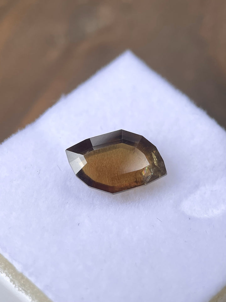 A 3.78-carat earthy brown cognac sapphire with a custom leaf portrait cut, displayed on a white velvet surface. The gemstone showcases warm brown hues and intricate facets. Sourced from the Umba River, Tanzania, the sapphire is untreated and measures 12.76mm by 4.78mm by 3.80mm.