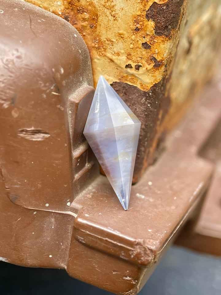 8.00 ct periwinkle sapphire resting on rusty metal, highlighting its clean lines, earthy tones, and symmetrical rhombohedral form.