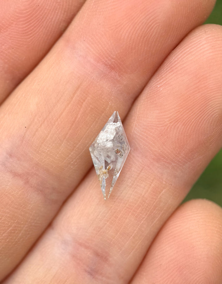 Close-up of a 2.85-carat untreated sapphire from Sri Lanka with a faceted rhombohedral cut and silvery gray color resting on fingertips.