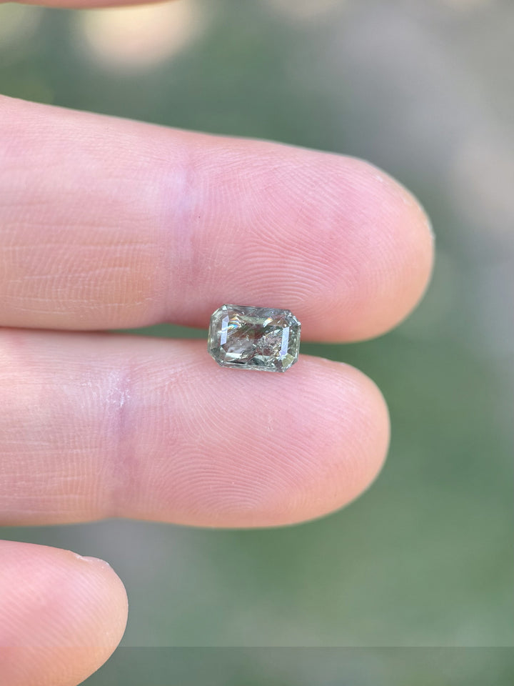 Natural teal and glitter green 2.06ct sapphire shown on fingertips, showcasing clarity and modified emerald cut