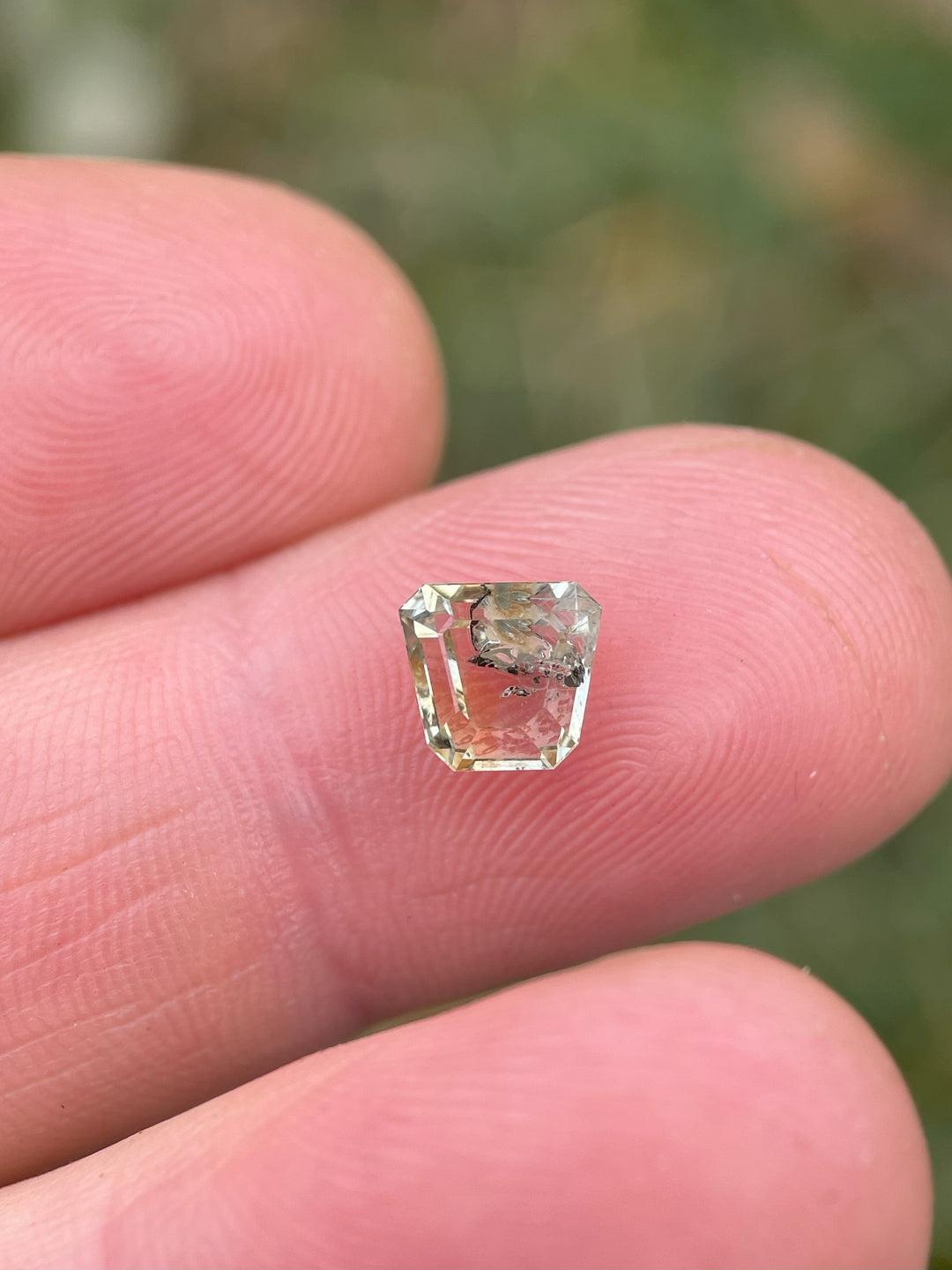 A 1.68-carat earthy yellow-green sapphire in a custom shield tablet cut, displayed on a fingertip to showcase its intricate details.