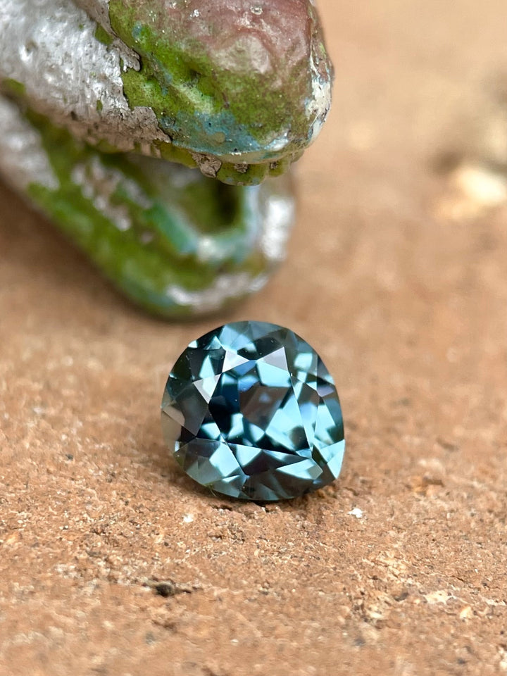 1.02ct Montana sapphire with teal and blue color tones, displayed on a rustic stone background.
