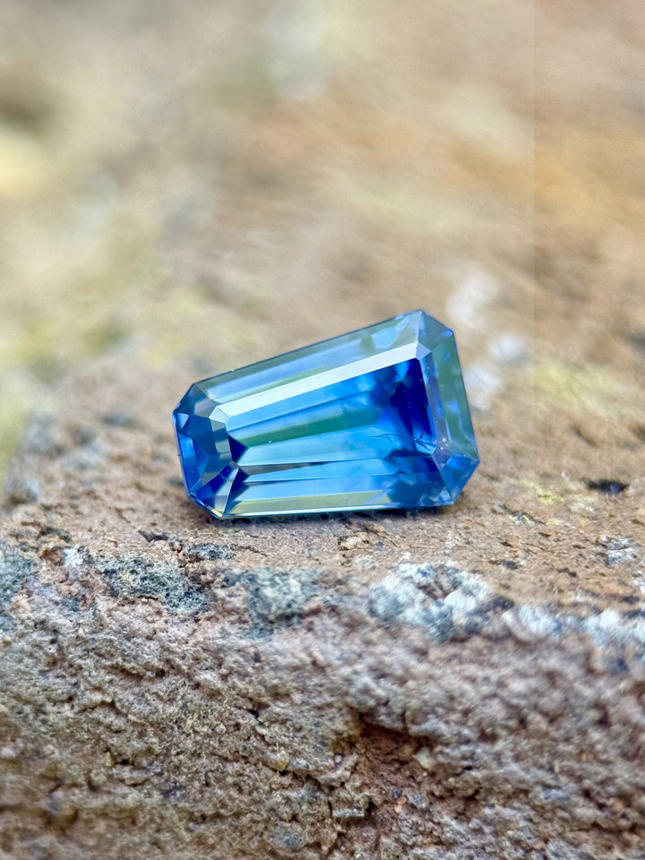 1.20 carat Montana sapphire with rich blue color and tapered shield step cut, resting on a textured rock background.