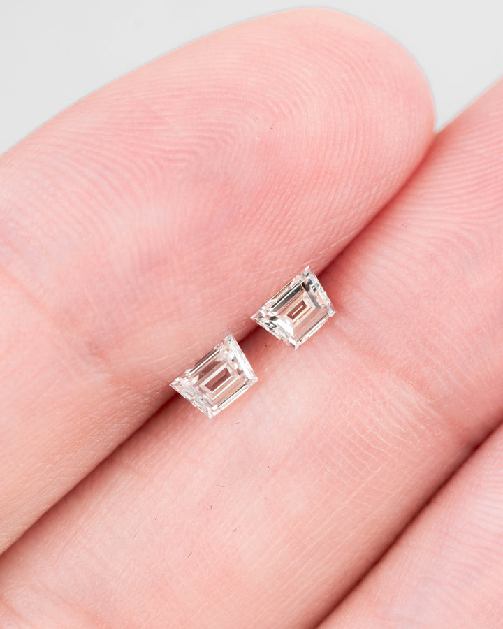 Matched pair of 0.37-carat G-color VVS–VS trapezoid step cut diamonds displayed on fingertips, showing the clarity, precise faceting, and symmetry of the natural South African stones with no treatment.
