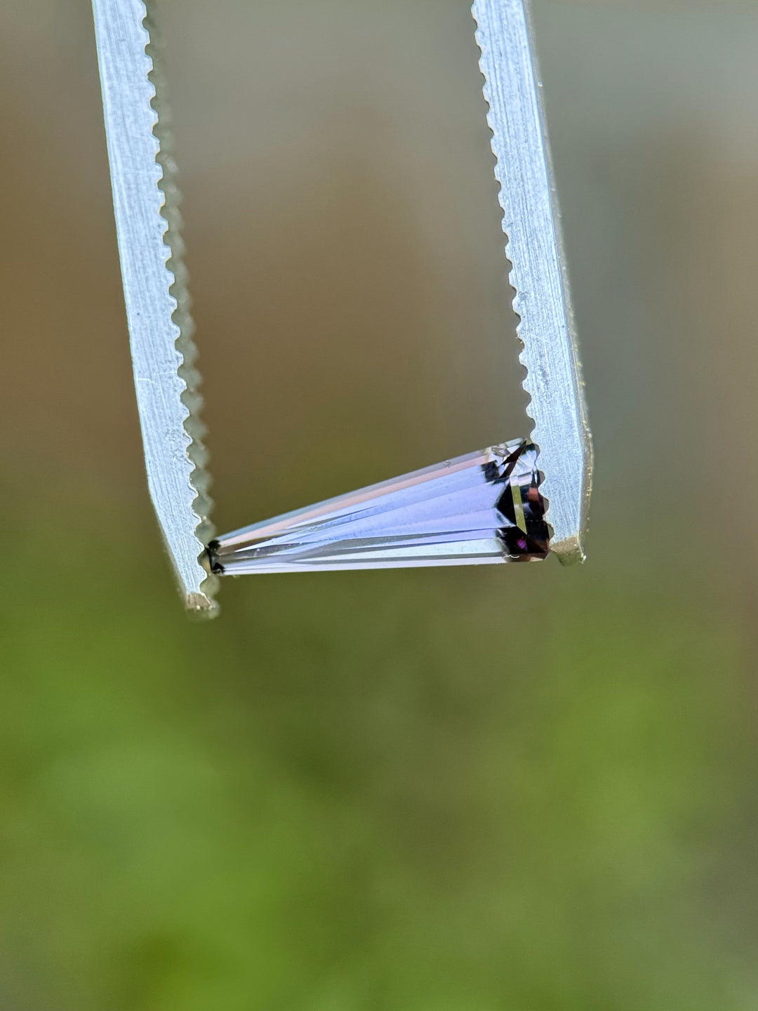 Close-up of a 0.67-carat Tanzanite held in tweezers, highlighting the step cut tapered baguette shape and color zoning.