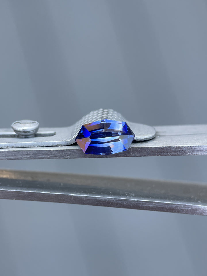 Bi-color sapphire held in tweezers, displaying its unique 1.03 carat custom geometric marquise cut, measured at 8.30 x 5.10 x 3.30 mm, from Sri Lanka, highlighted against a subdued background.