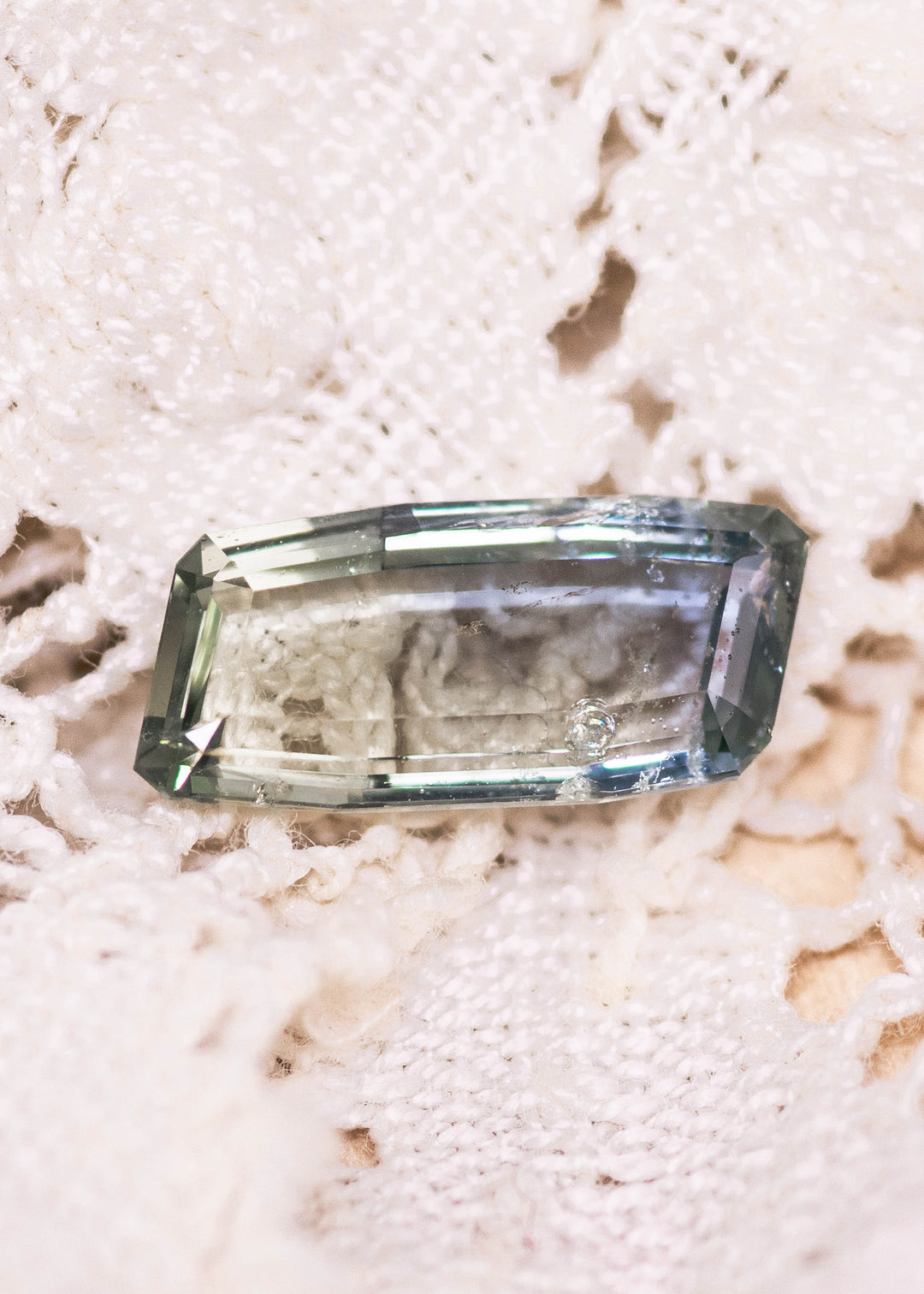 Unheated 2.31CT yellow green teal sapphire photographed on a textured natural surface, highlighting the elongated baguette portrait cut, step facets, and clarity from Umba River, Tanzania