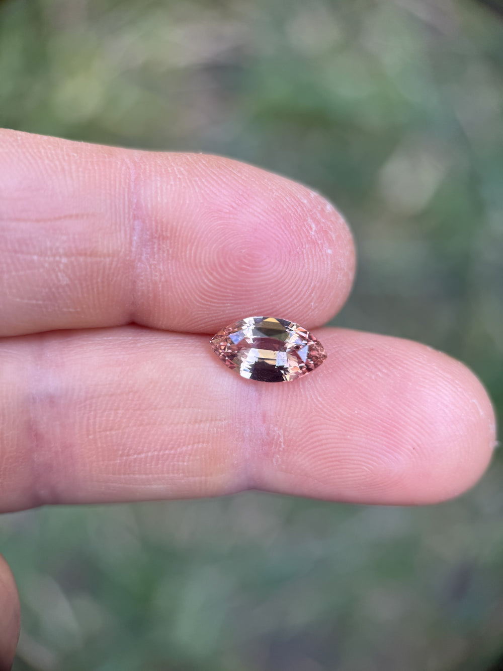 2.57ct peach pink rose-champagne marquise sapphire displayed on a fingertip to show size and clarity, precision mixed cut sparkling in natural daylight; untreated sapphire from Sakaraha, Madagascar.