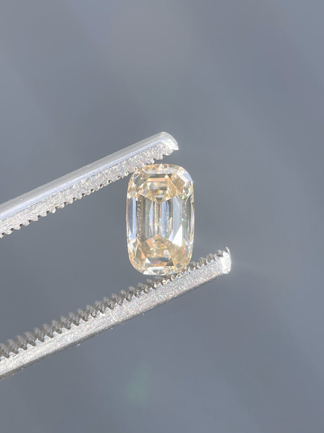 Close-up of a 1.03-carat antique-style elongated cushion cut diamond with champagne and light fancy yellowish brown hues, held by precision tweezers against a neutral background.