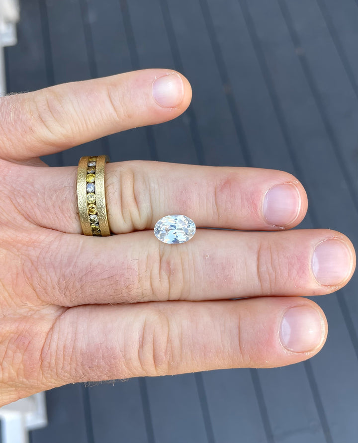 Natural opalescent white sapphire weighing 4.23 carats in an oval brilliant cut, showcased on fingers with detailed clarity.