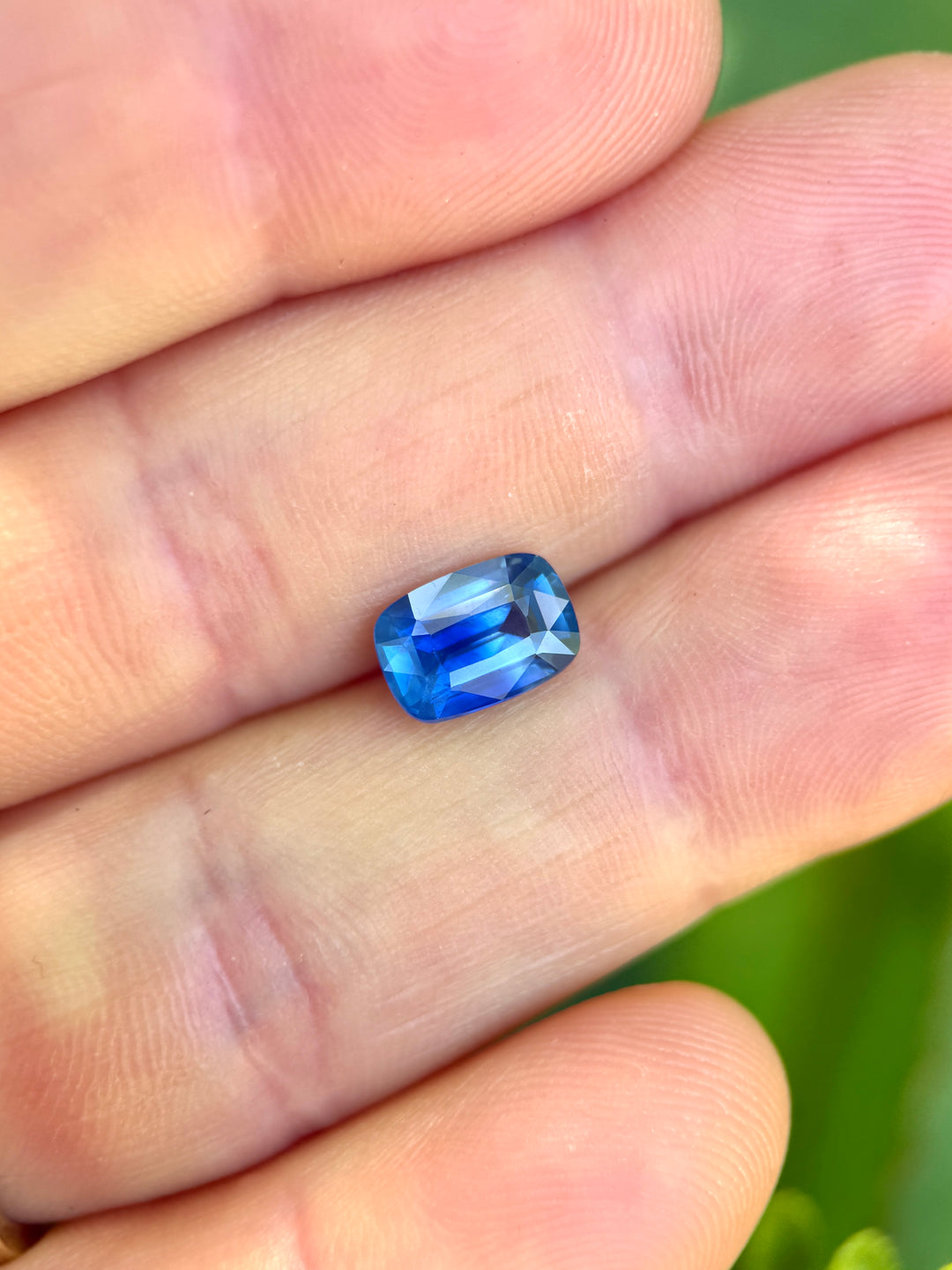 Elongated cushion cut parti sapphire resting on fingertips, showing opalescent blue glow and contrasting cornflower-to-royal blue color distribution.