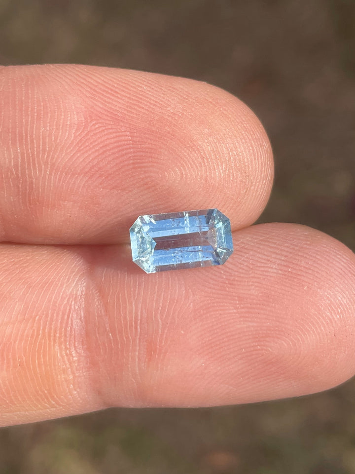 1.72 carat emerald-cut aquamarine gemstone in seafoam green and blue hues, displayed on a finger for scale.