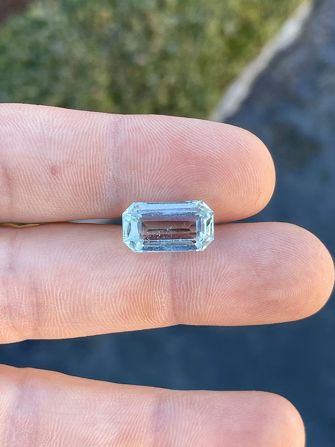 Emerald-cut aquamarine gemstone weighing 8.80 carats resting on fingertips, displaying its natural mint blue-green tones.