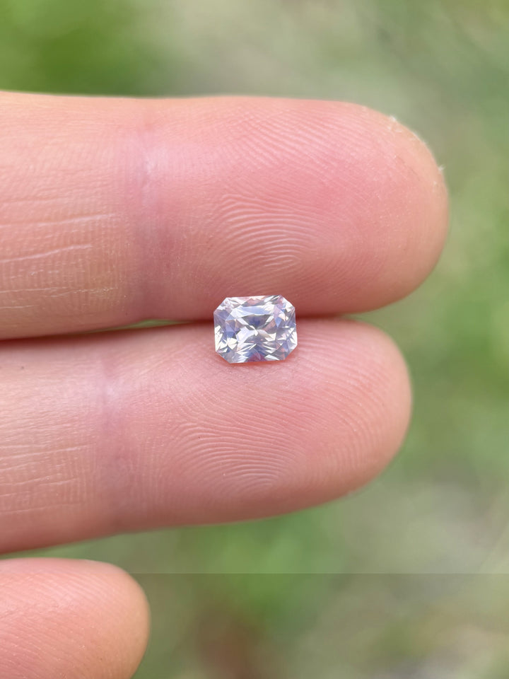 1.18-carat unheated bi-color sapphire with lilac and lavender hues resting on a fingertip, showcasing its brilliance and clarity – Ratnapura, Sri Lanka