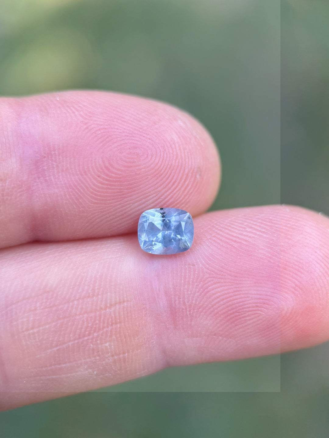 Periwinkle blue 1.22ct Montana sapphire resting on fingertip, showcasing custom elongated cushion cut and clarity