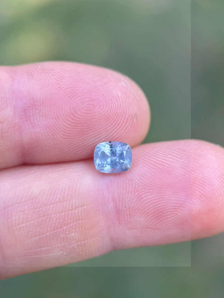 Periwinkle blue 1.22ct Montana sapphire resting on fingertip, showcasing custom elongated cushion cut and clarity