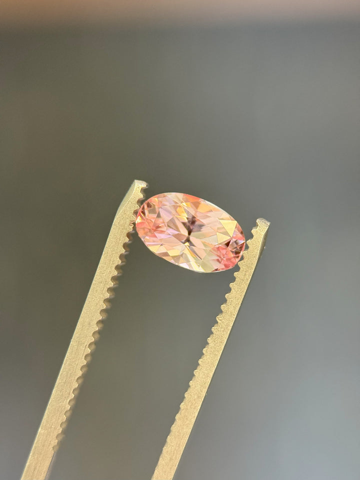 Salmon pink sapphire in tweezers with radiant sparkle and vivid color from Madagascar