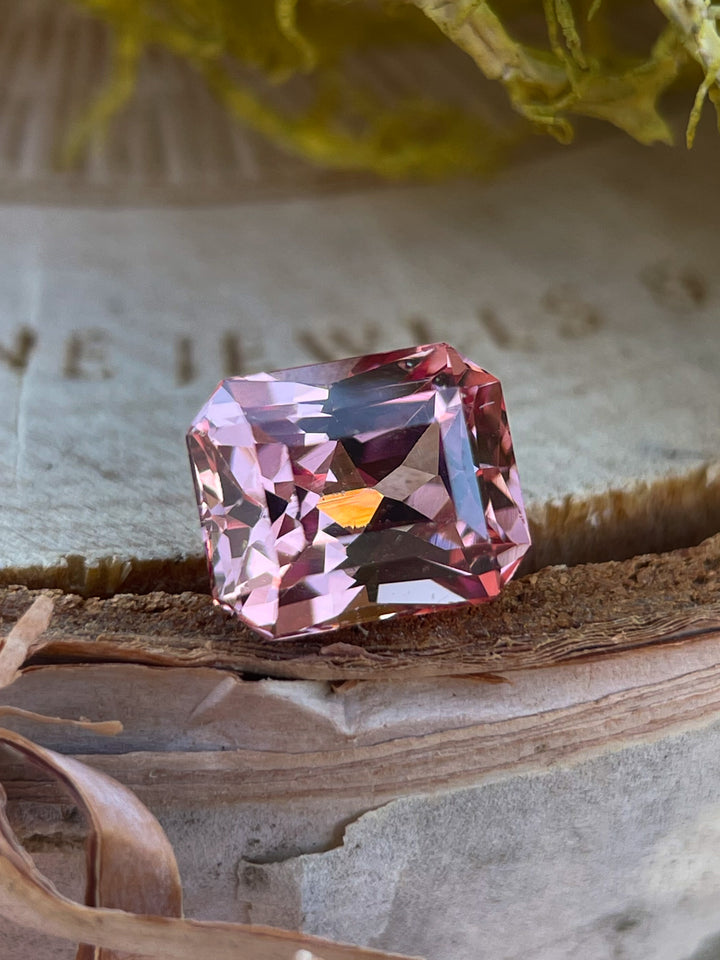 An elegant 1.45-carat peach champagne garnet displayed on natural wood, featuring a modified octagonal step cut, sourced from Madagascar.