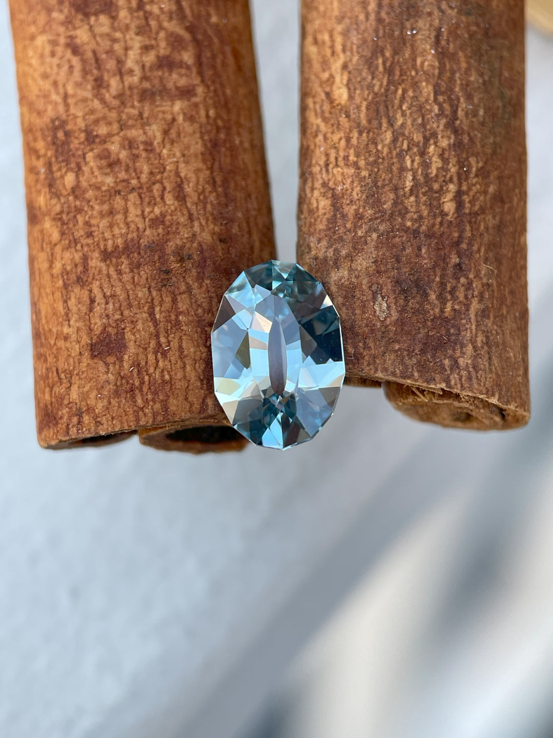 Elegant seafoam blue sapphire weighing 1.61 carats, with a mix brilliant oval cut, resting against cinnamon sticks.