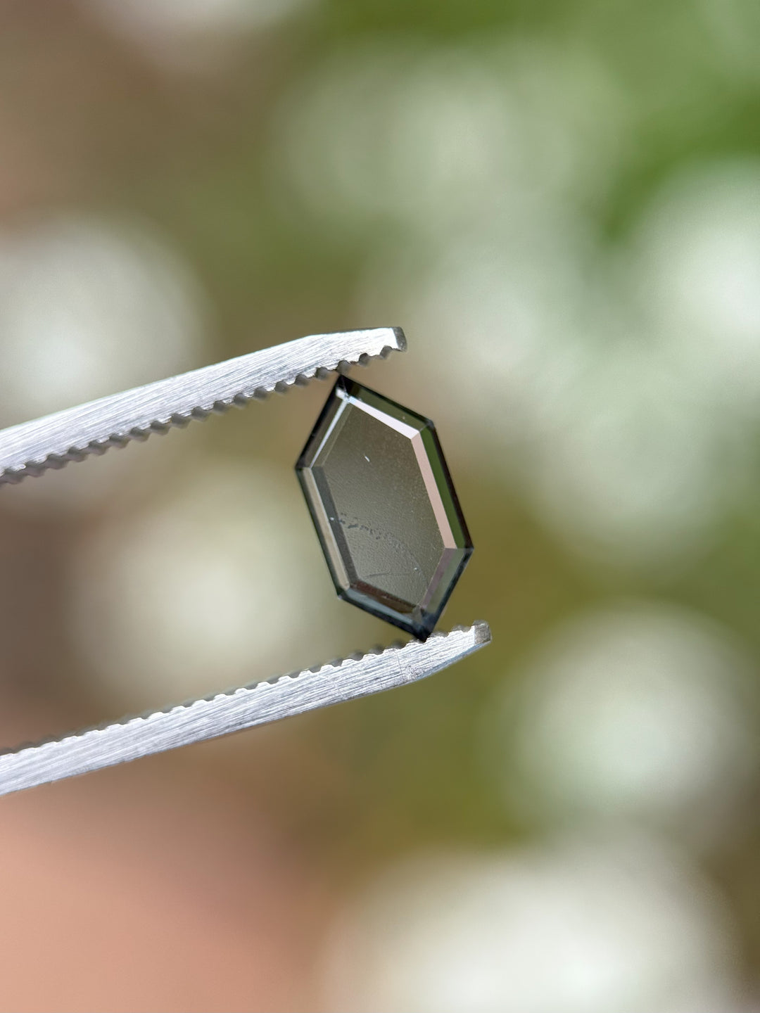 Side view of hex portrait cut spinel gemstone in tweezers showing depth and clarity