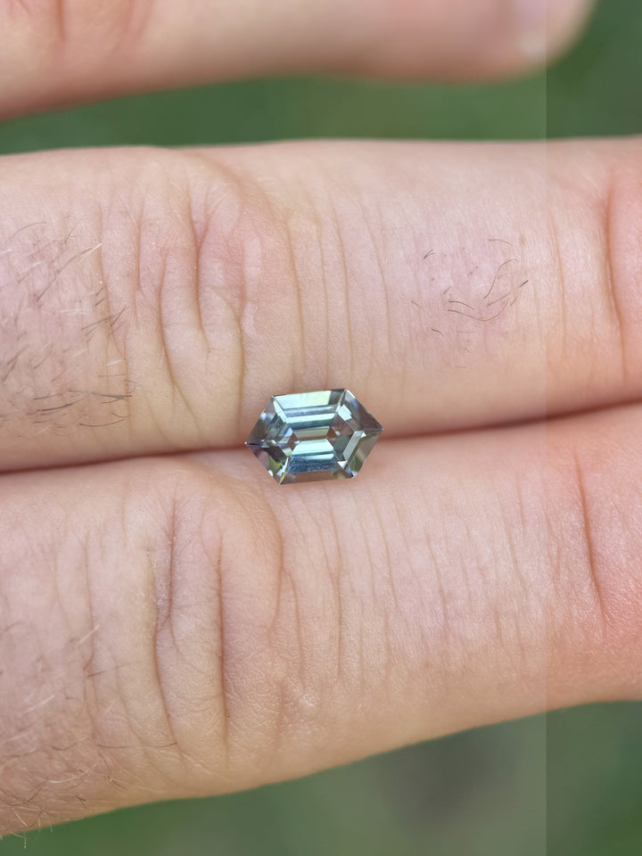 1.14ct Tanzanite on finger for scale, featuring vivid teal and purple mermaid hues with a clean step-cut hexagon profile