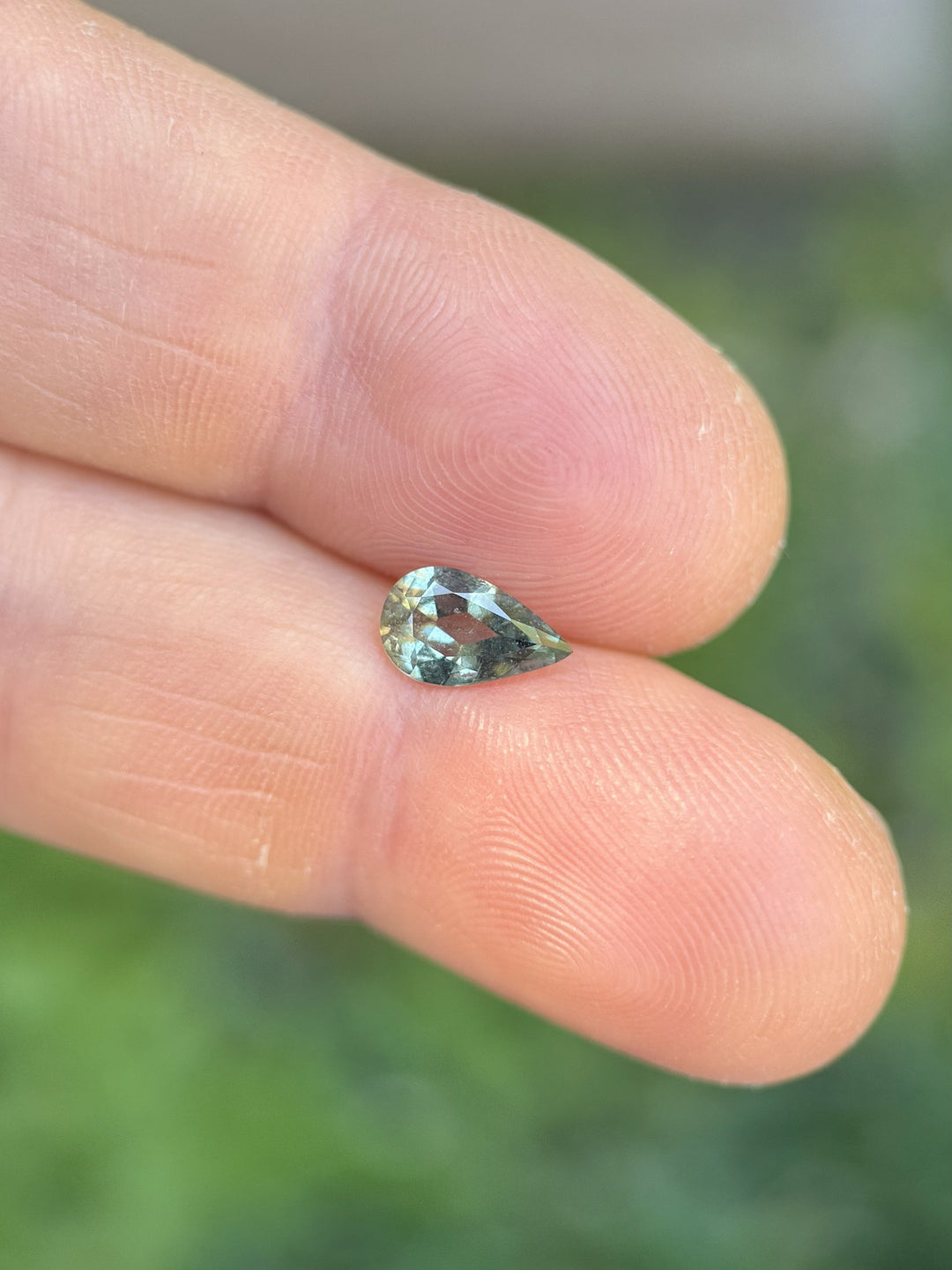 Loose 1.06ct sage green sapphire in modified pear brilliant cut displayed on fingertip, ethically sourced from Umba River, Tanzania
