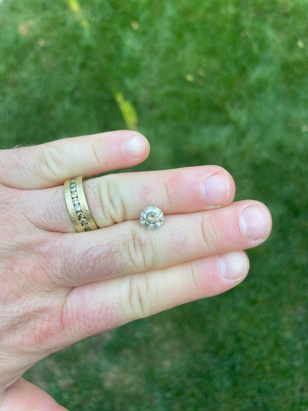 2.53-carat Fancy Gray round brilliant diamond held between fingers, showcasing its lustrous cut and unique shade, sourced from South Africa, against a natural green grass backdrop.